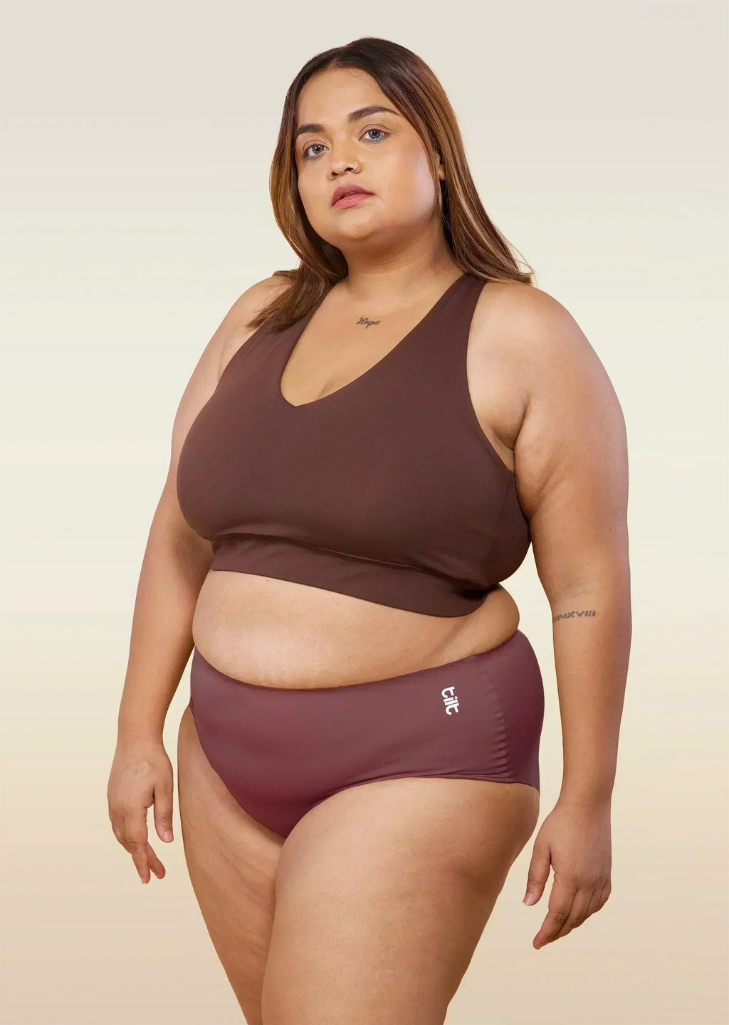 Woman wearing pink underwear and brown sports bra with a beige background