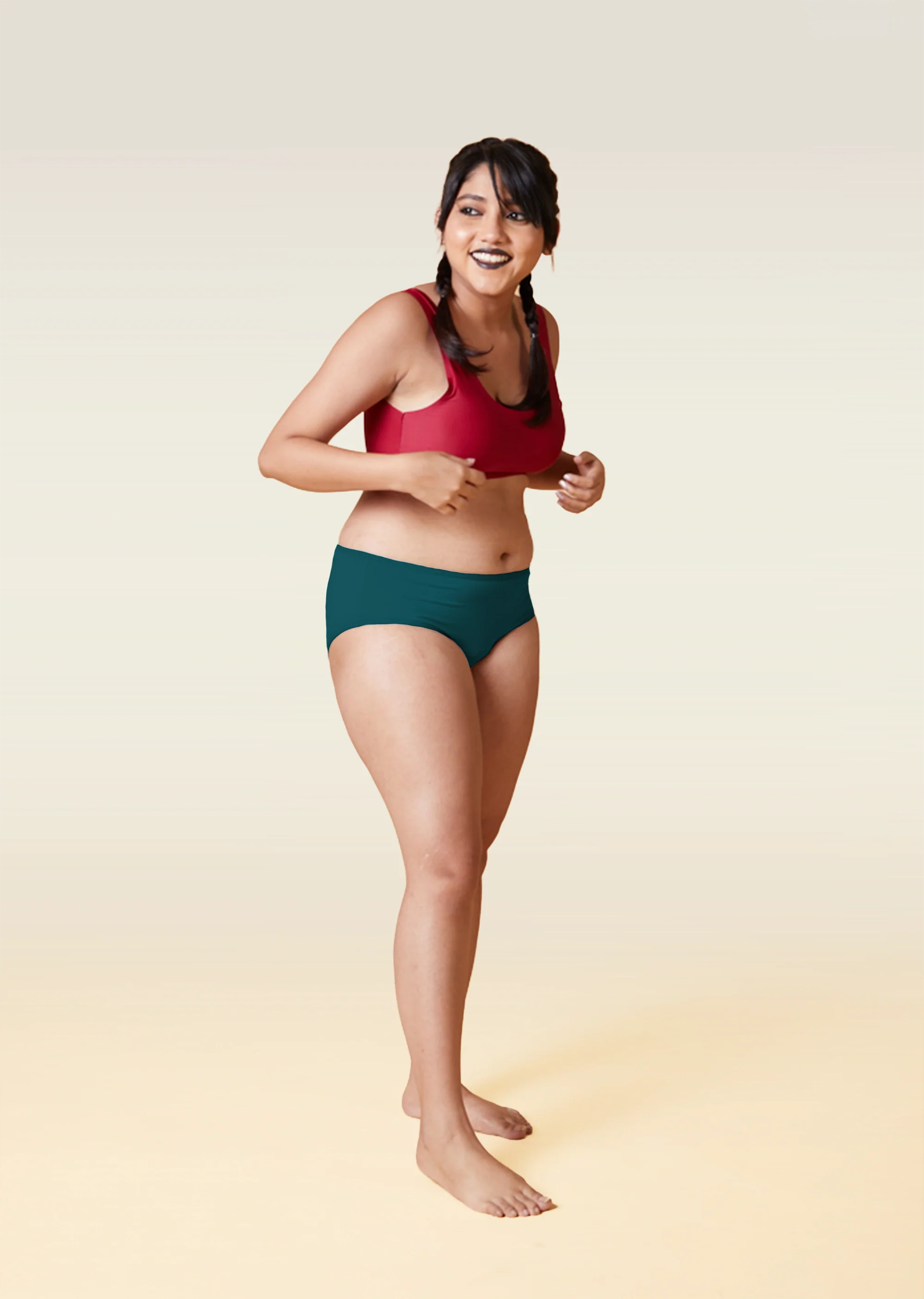 Woman wearing a red sports bra and teal underwear on a beige background 