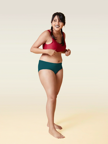 Woman wearing a red sports bra and teal underwear on a beige background 