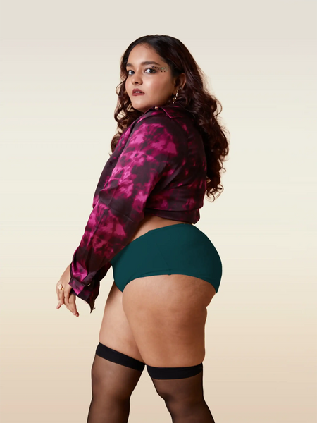 Woman wearing a pink and black patterned jacket, teal underwear, and black stockings on a beige background