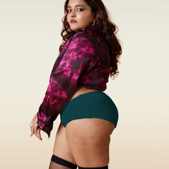Woman wearing a pink and black patterned jacket, teal underwear, and black stockings on a beige background