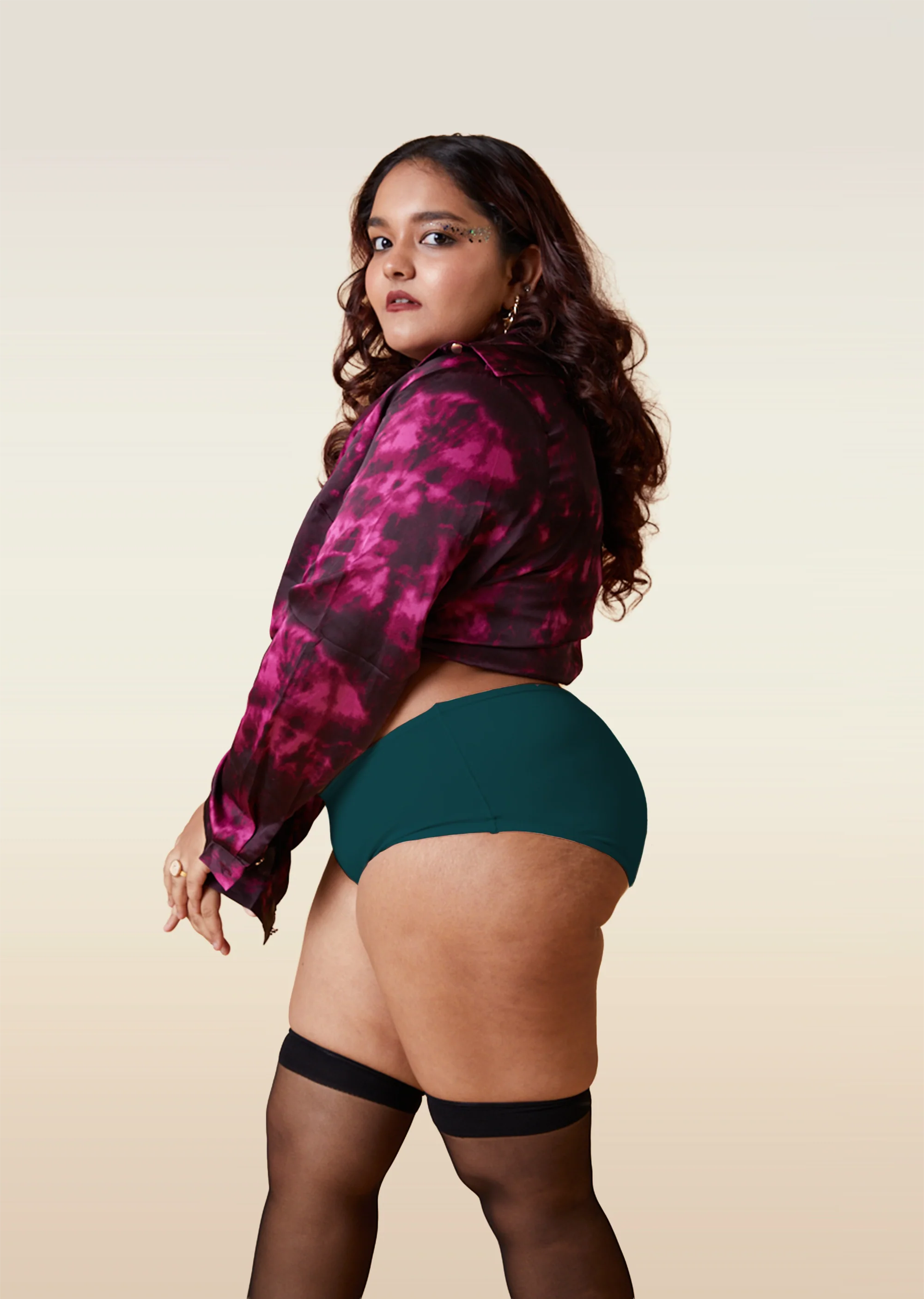 Woman wearing a pink and black patterned shirt with teal underwear and black stockings on a beige background