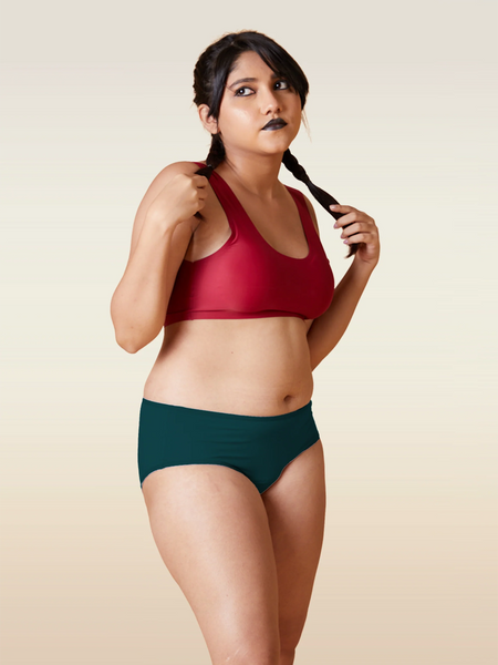 Woman wearing a red sports bra and teal mid-waist underwear against a beige background