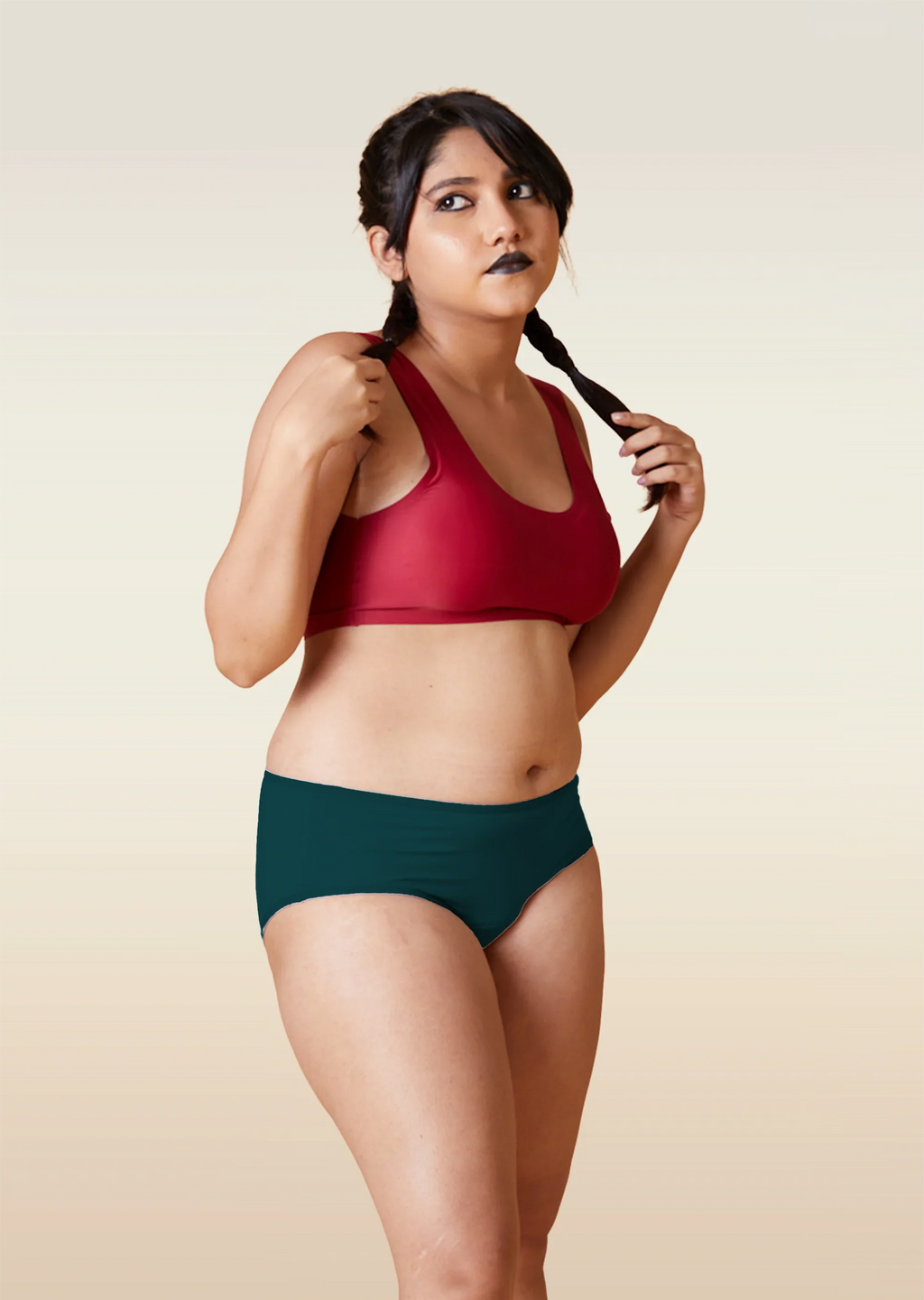Woman wearing a red sports bra and teal mid-waist underwear against a beige background