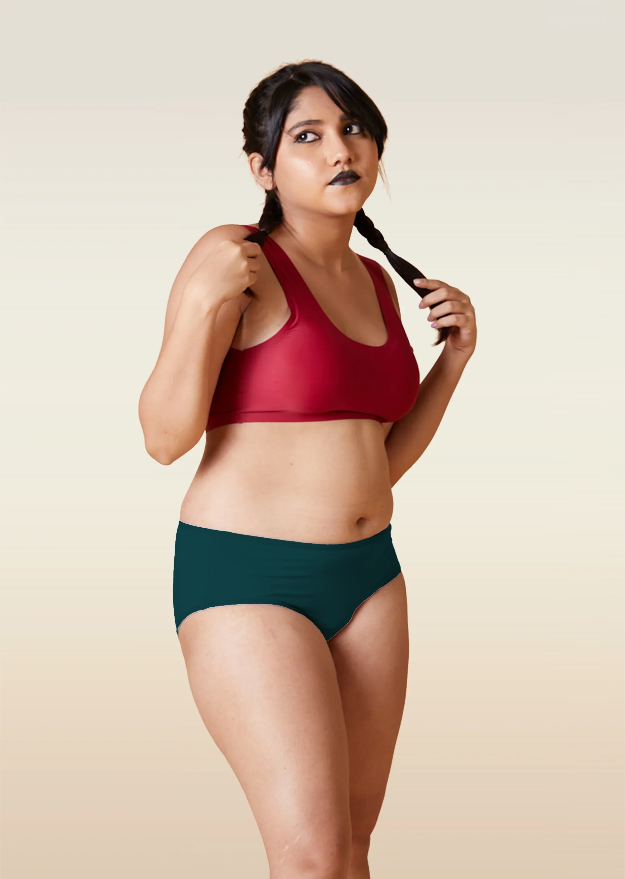 Woman wearing a red sports bra and teal mid-waist underwear against a beige background