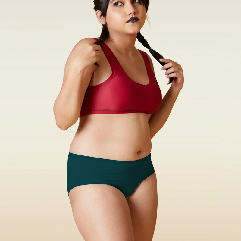 Woman wearing a red sports bra and teal mid-waist underwear against a beige background