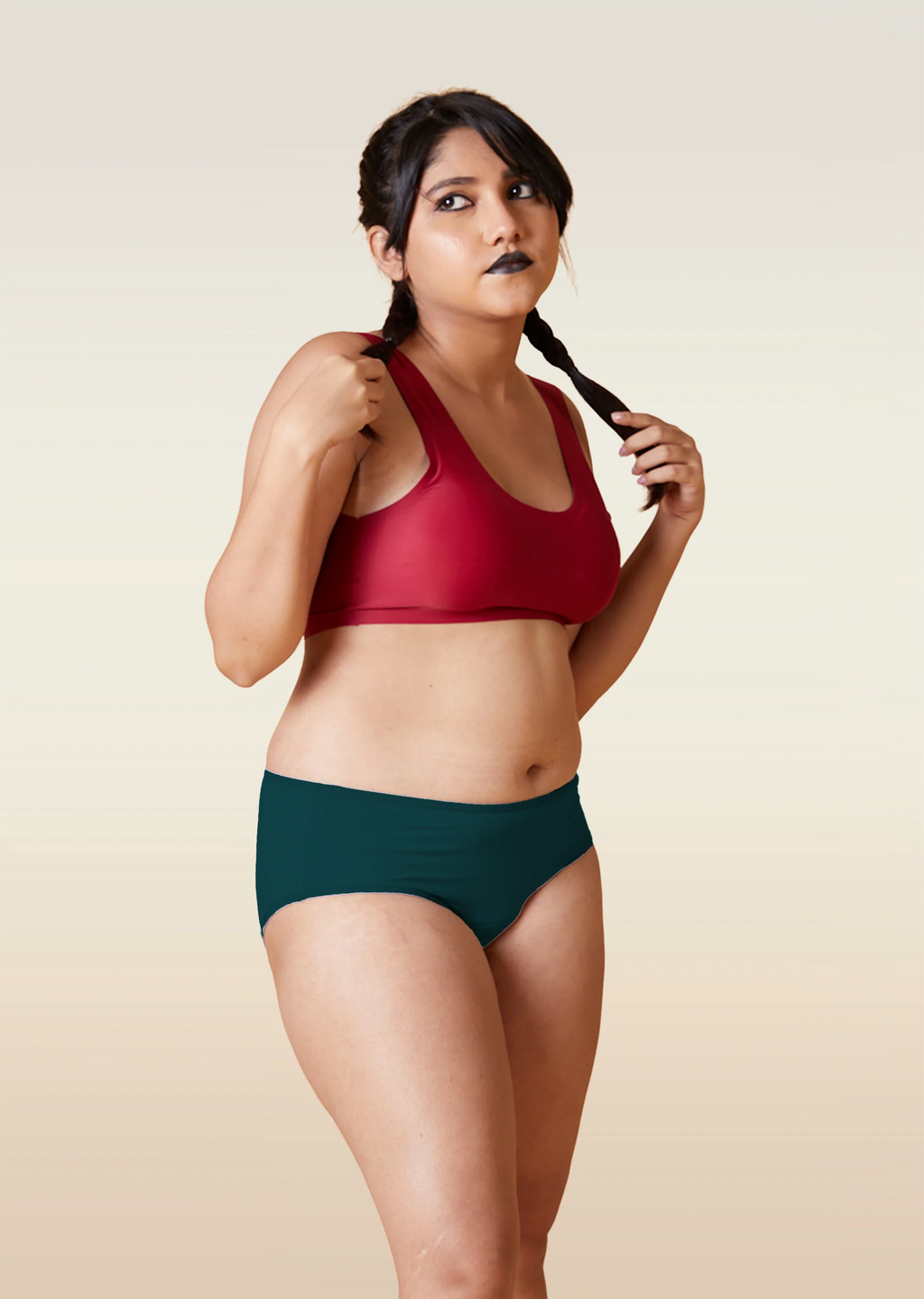 Woman wearing a red sports bra and teal mid-waist underwear against a beige background