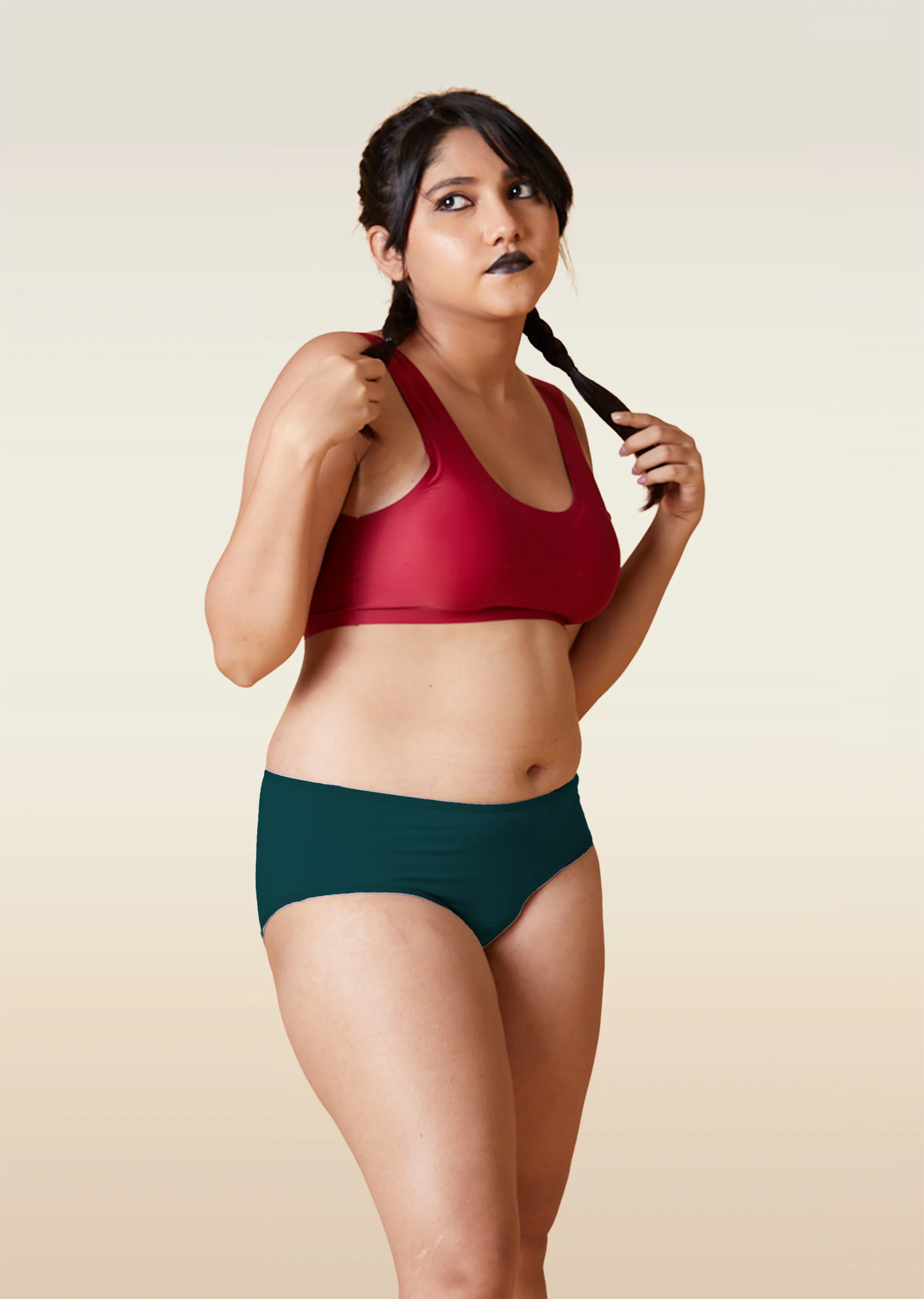Woman wearing a red sports bra and teal mid-waist underwear against a beige background