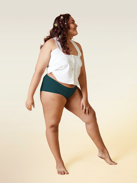 Woman wearing a white top and teal underwear on a beige background