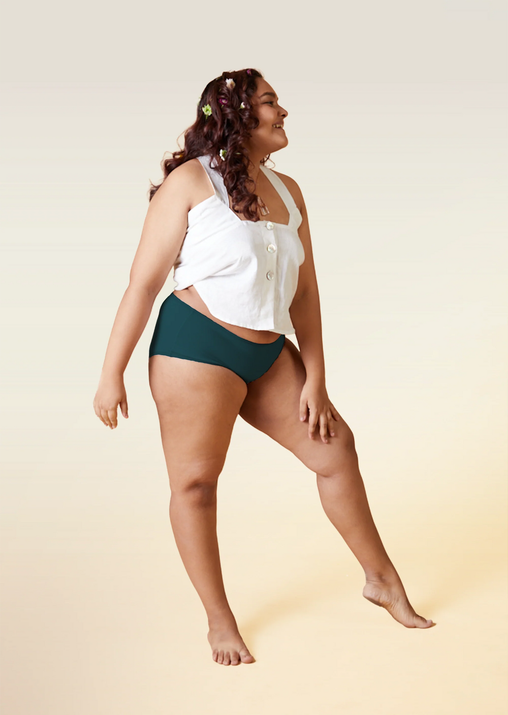 Woman wearing a white top and teal underwear on a beige background