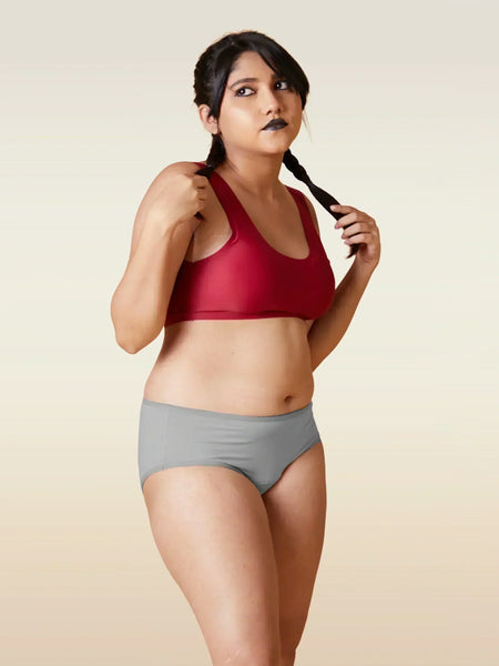 Woman wearing a red sports bra and gray underwear on a beige background