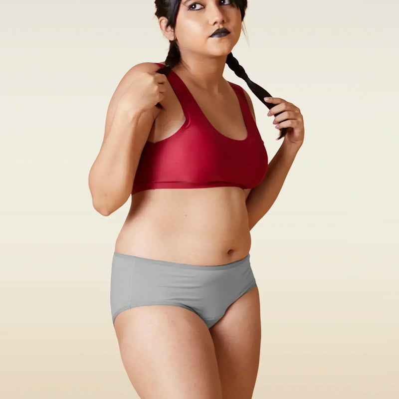 Woman wearing a red sports bra and gray underwear on a beige background