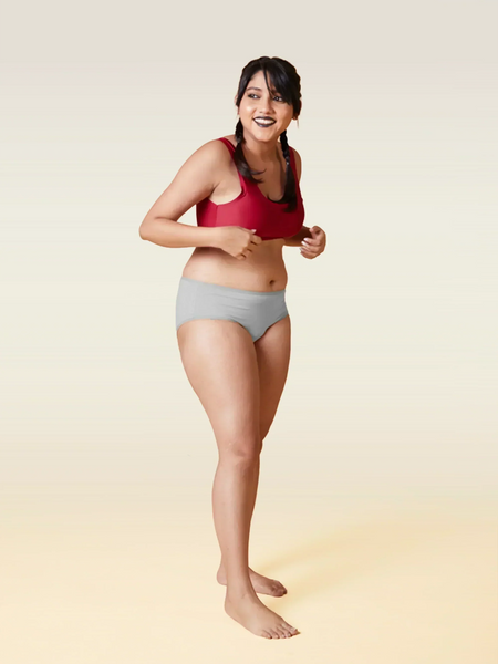 Woman wearing a red sports bra and gray underwear on a gradient background