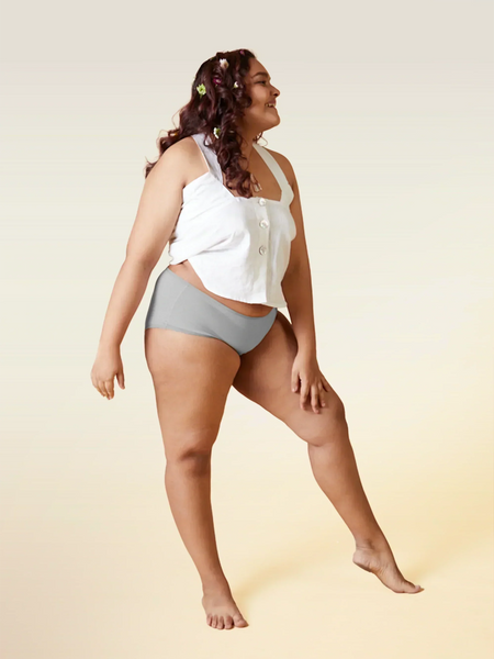 Woman wearing a white top and gray underwear on a beige background