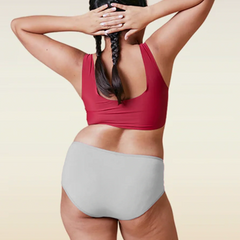 Person wearing a red sports bra and gray mid-waisted underwear on a beige background