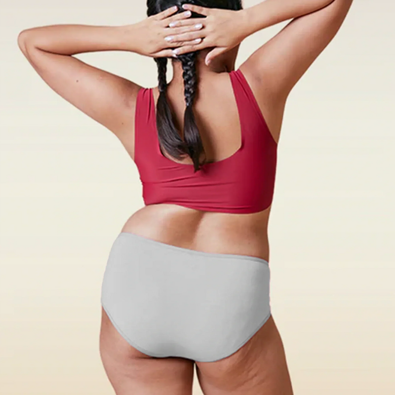 Person wearing a red sports bra and gray mid-waisted underwear on a beige background
