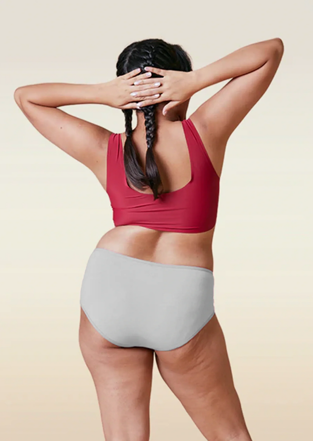 Person wearing a red sports bra and gray mid-waisted underwear on a beige background