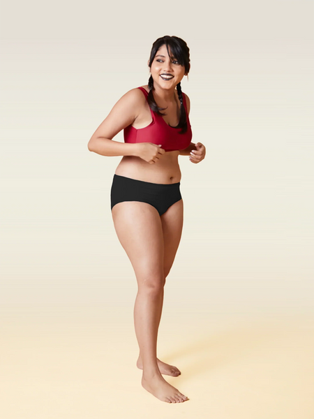 Woman wearing a red sports bra and black briefs on a gradient background
