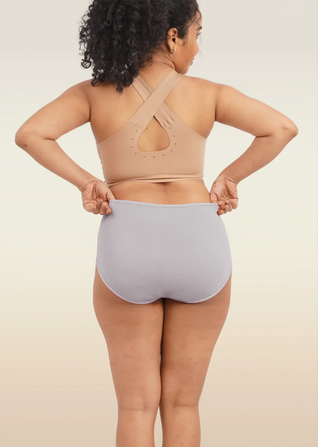 Person wearing a beige sports bra and light gray high-waisted underwear on a plain background
