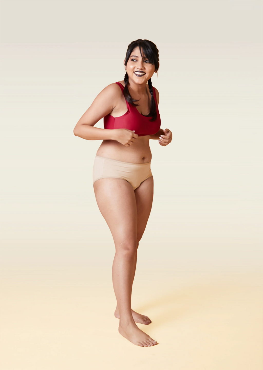 Woman wearing a red sports bra and beige underwear on a beige background