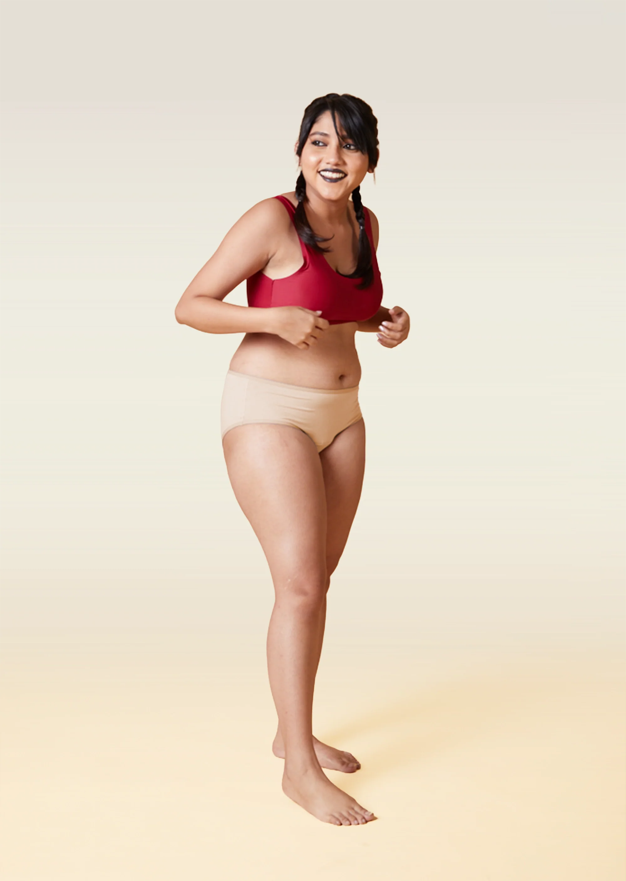 Woman wearing a red sports bra and beige underwear on a beige background