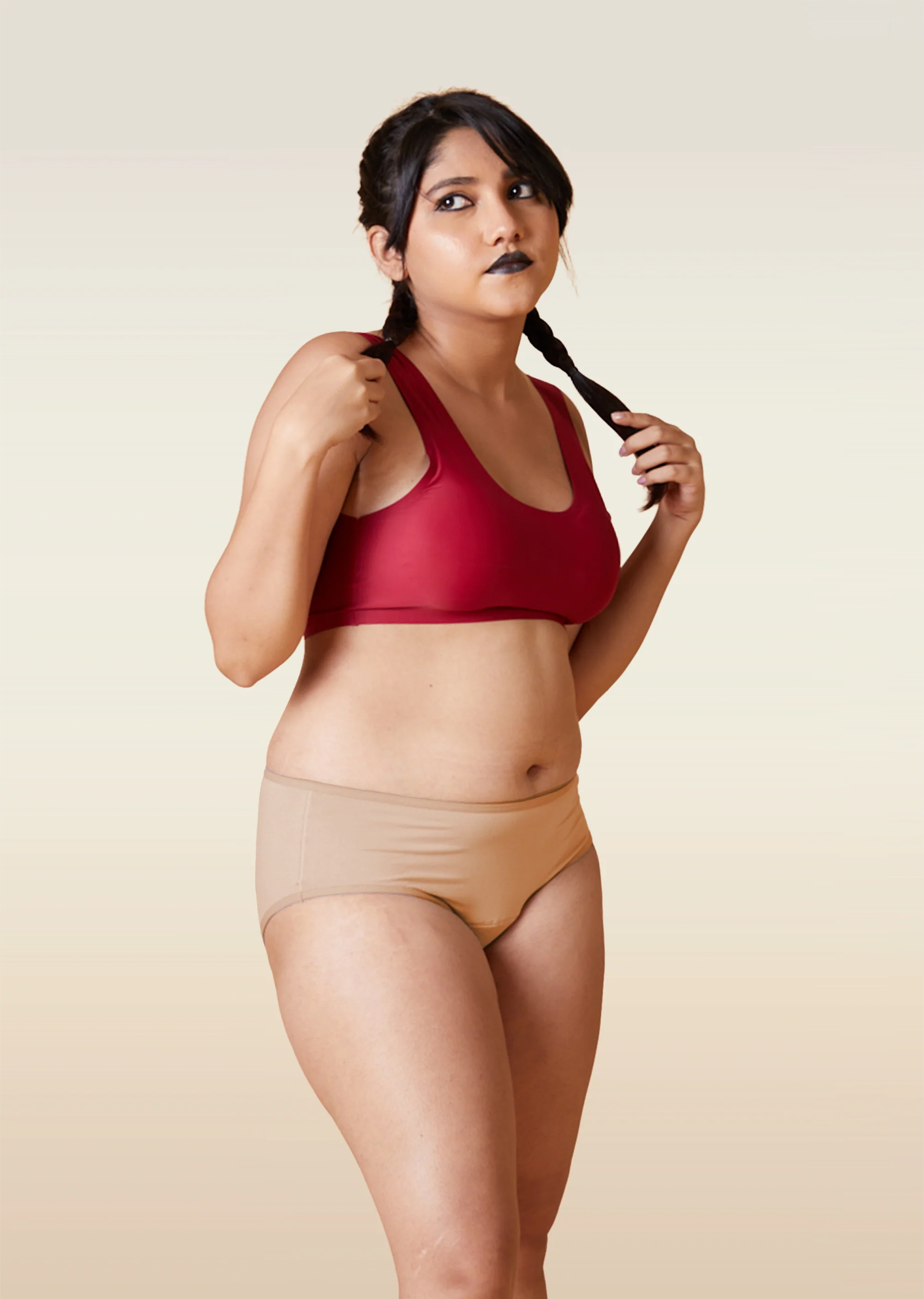 Woman wearing a red sports bra and beige underwear on a beige background