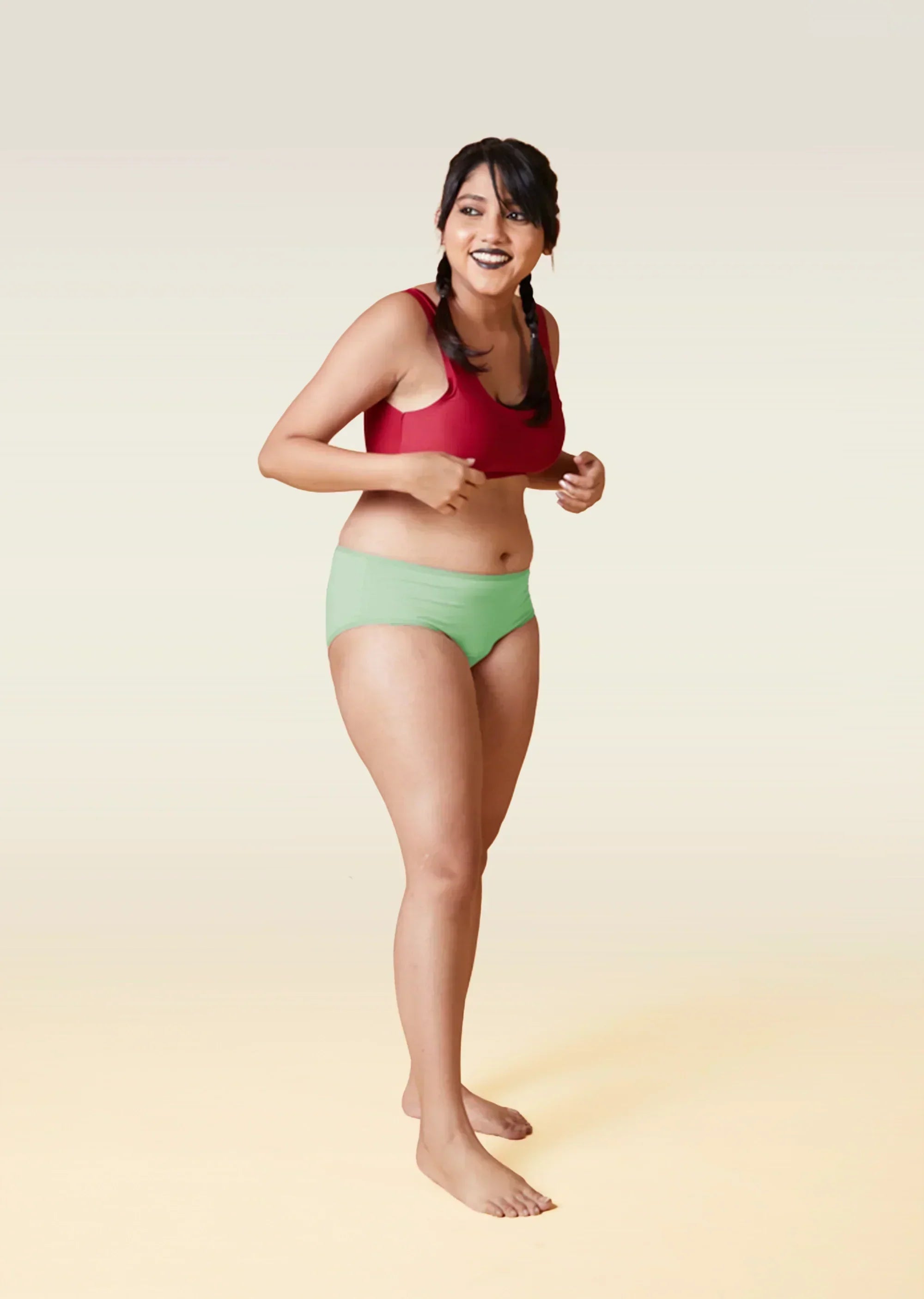 Woman wearing a red sports bra and green underwear on a gradient background
