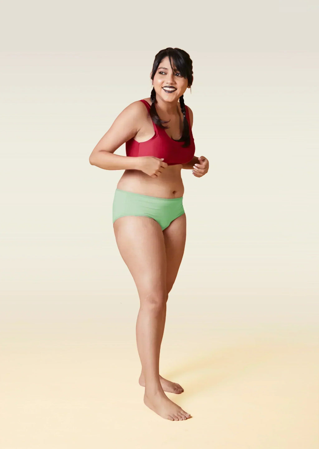 Woman wearing a red sports bra and green underwear on a gradient background