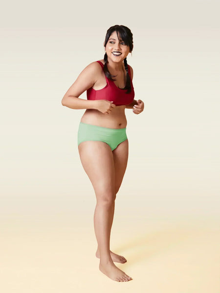Woman wearing a red sports bra and green underwear on a gradient background