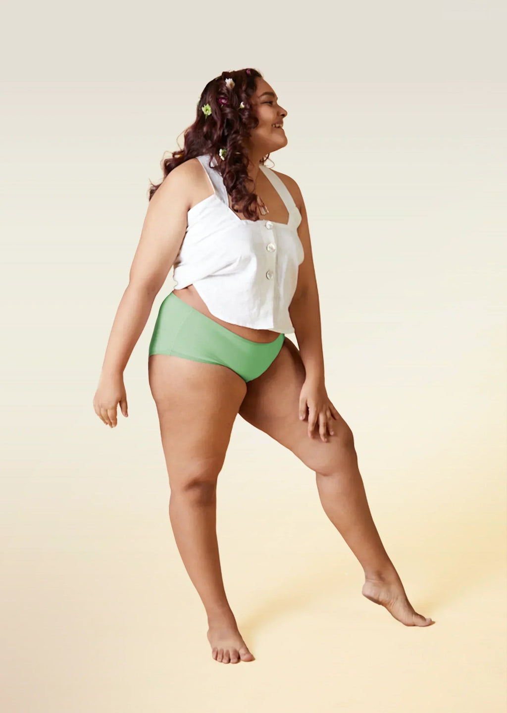 Woman wearing a white top and green underwear on a gradient background