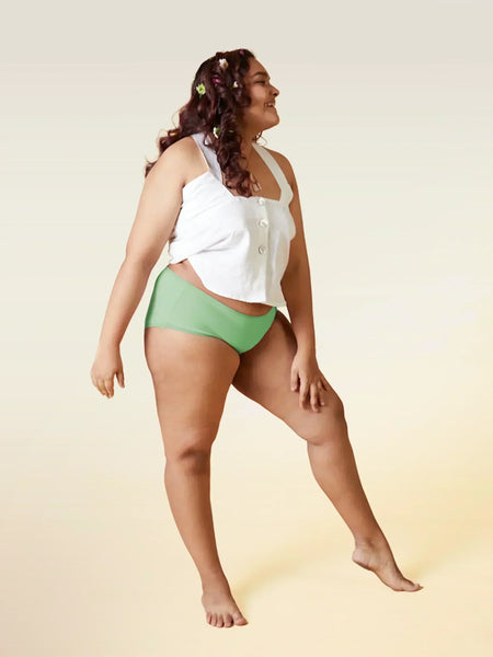 Woman wearing a white top and green underwear on a gradient background
