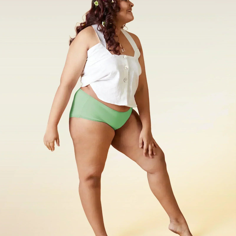 Woman wearing a white top and green underwear on a gradient background