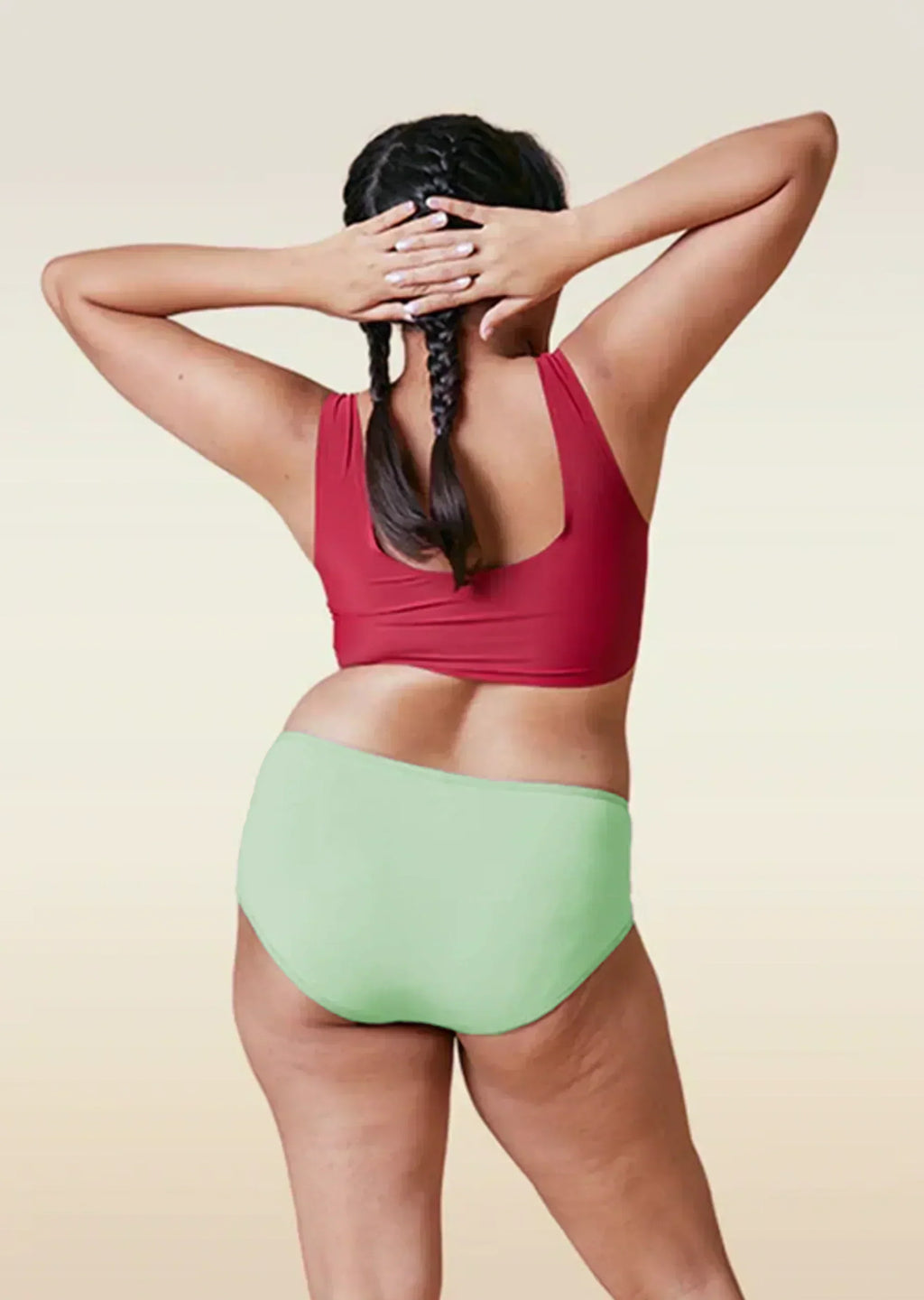 Person wearing a red top and green high-waisted bikini bottom on a beige background