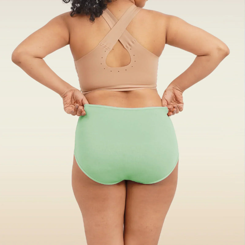 Person wearing a beige sports bra and green high-waisted breifs on a neutral background