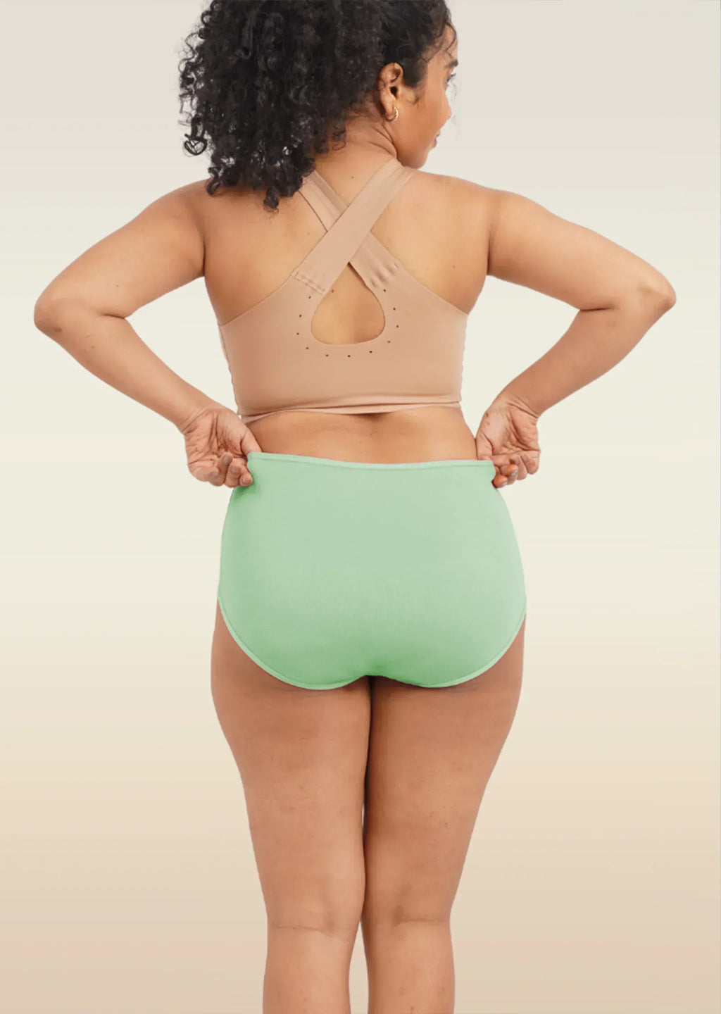 Person wearing a beige sports bra and green high-waisted breifs on a neutral background