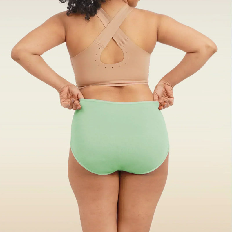 Person wearing a beige sports bra and green high-waisted breifs on a neutral background