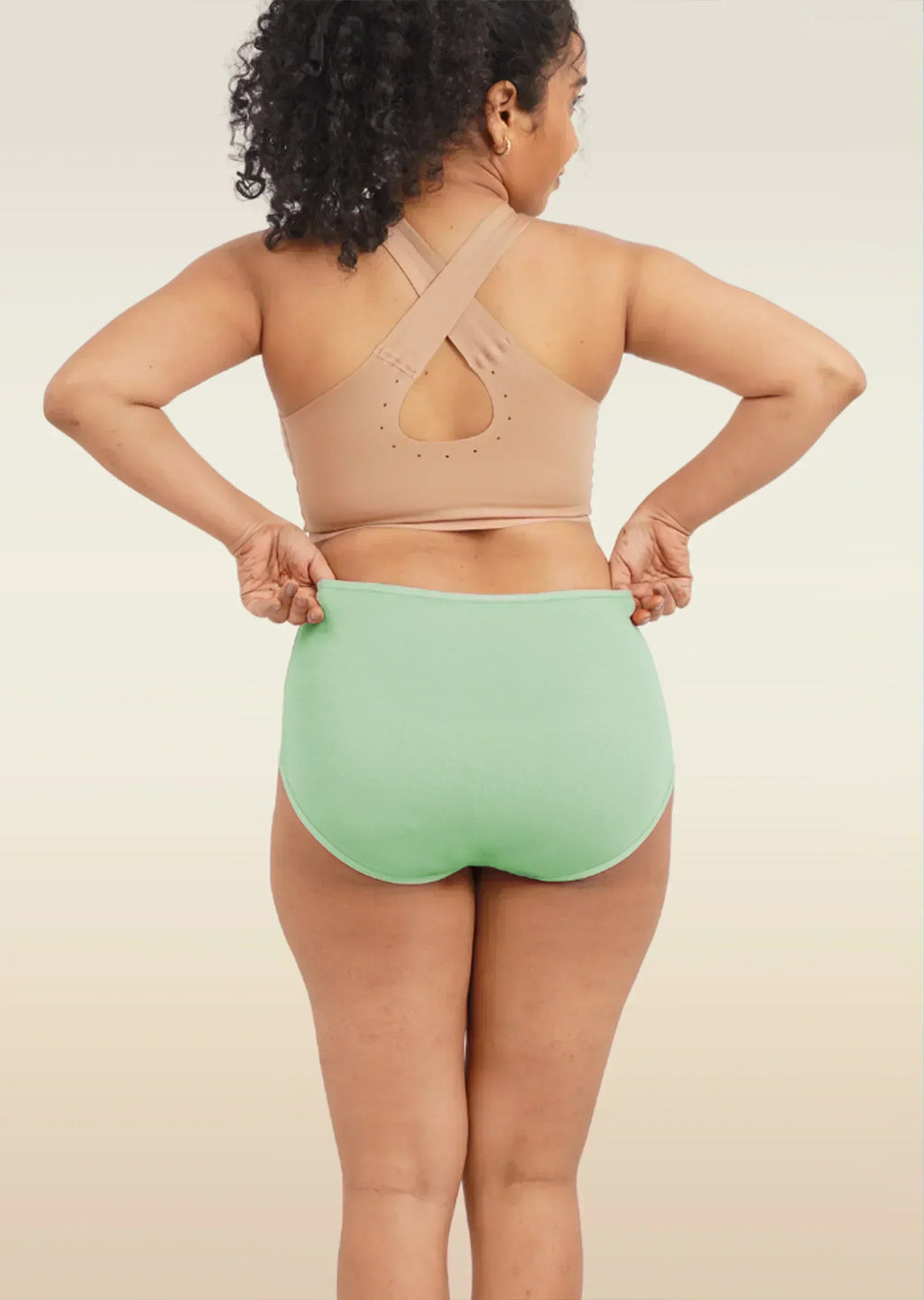 Person wearing a beige sports bra and green high-waisted breifs on a neutral background