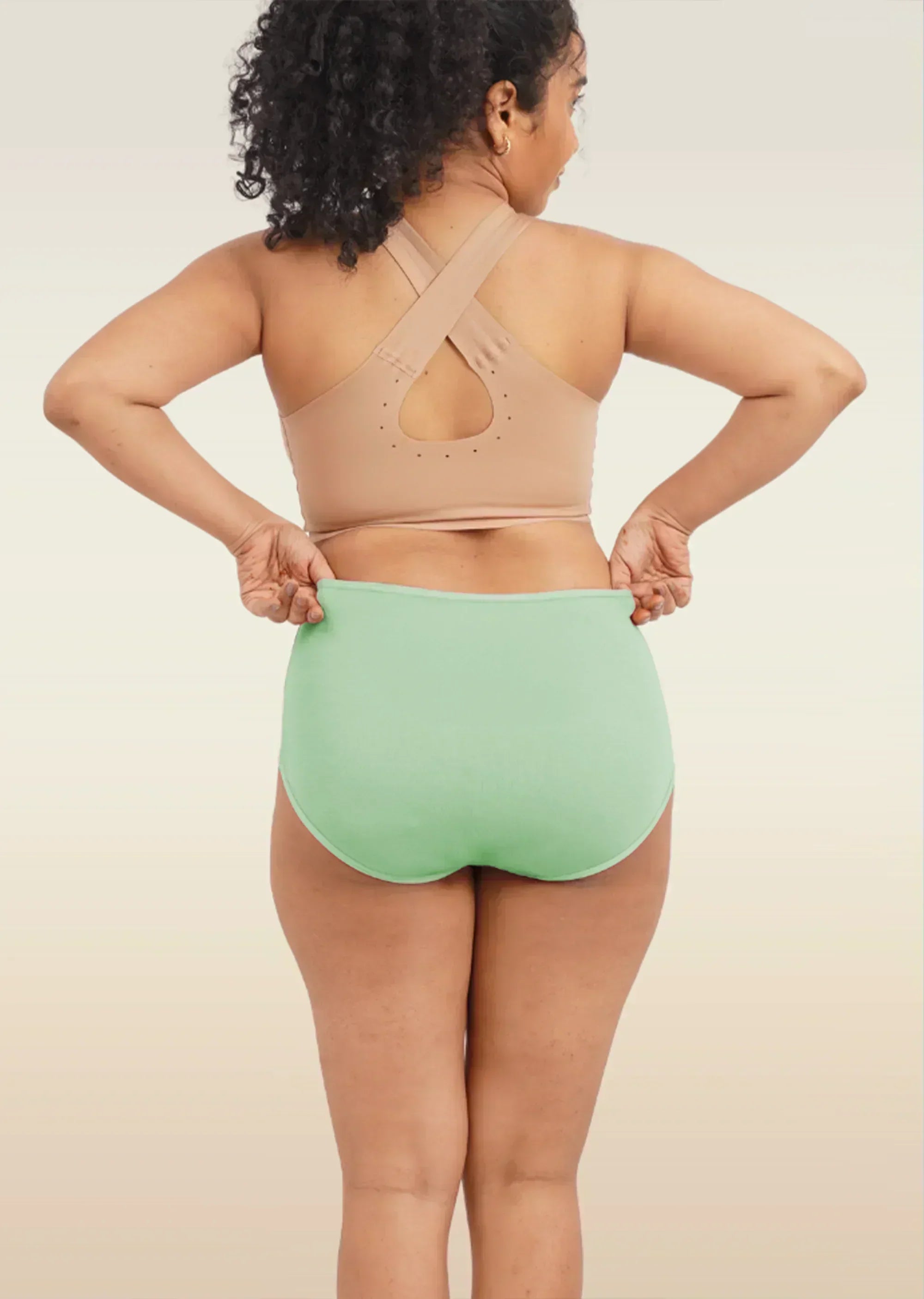 Person wearing a beige sports bra and green high-waisted breifs on a neutral background
