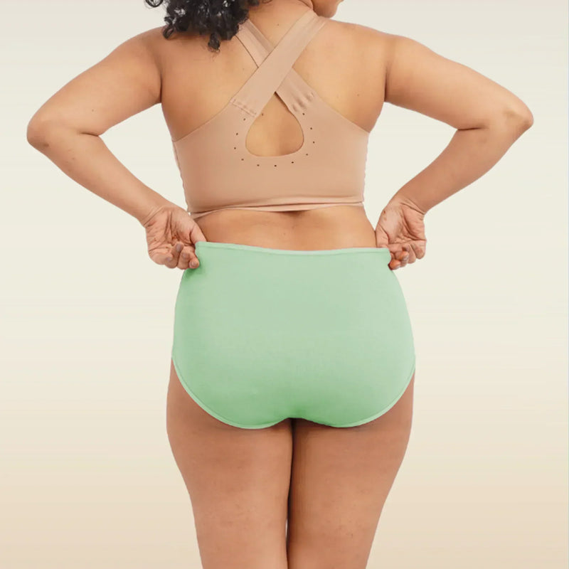 Person wearing a beige sports bra and green high-waisted breifs on a neutral background