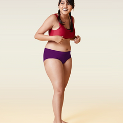 Woman wearing a red sports bra and violet mid-waist underwear  on a beige  background