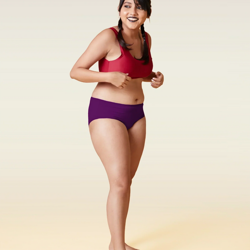 Woman wearing a red sports bra and violet mid-waist underwear  on a beige  background