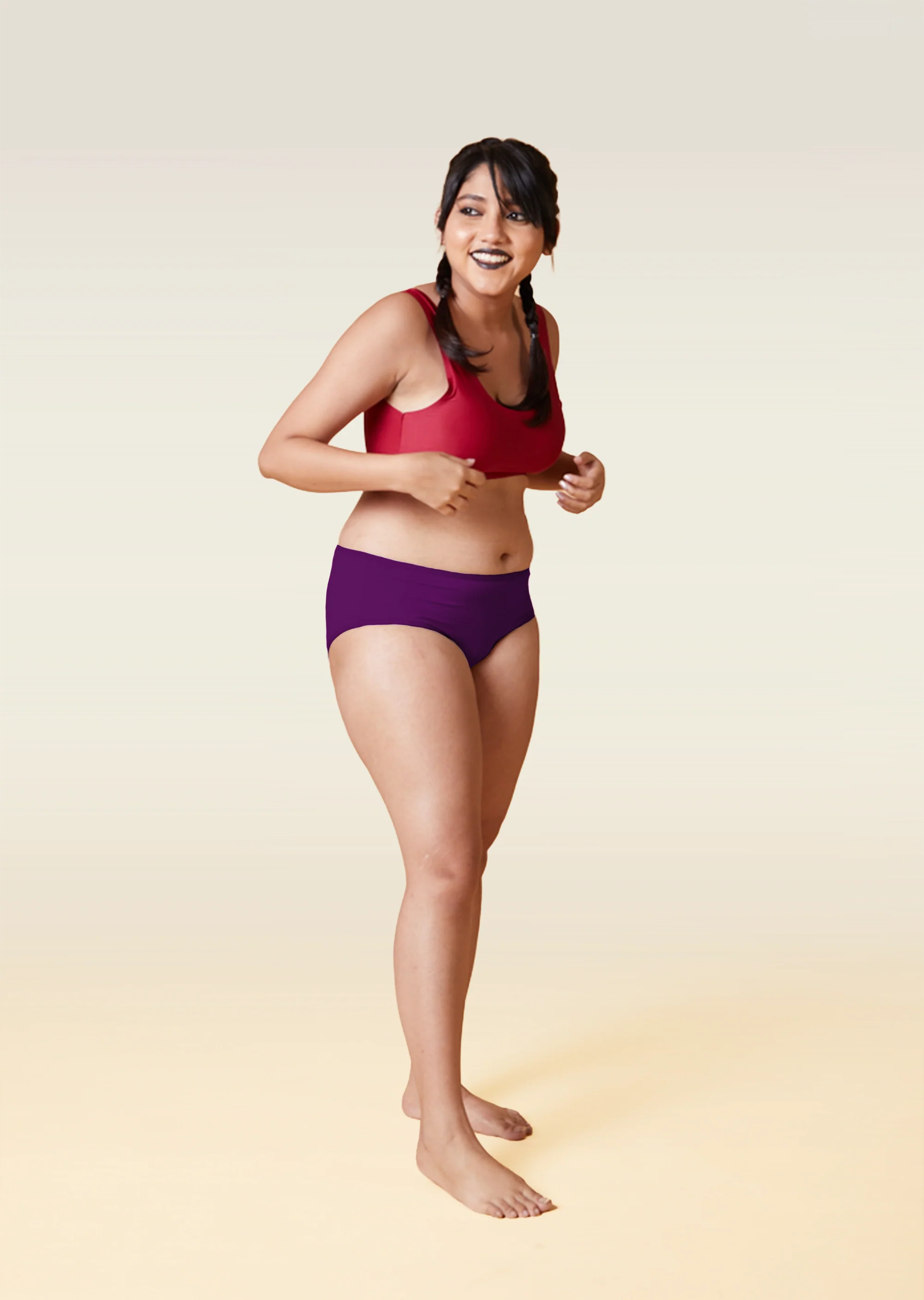 Woman wearing a red sports bra and violet mid-waist underwear  on a beige  background