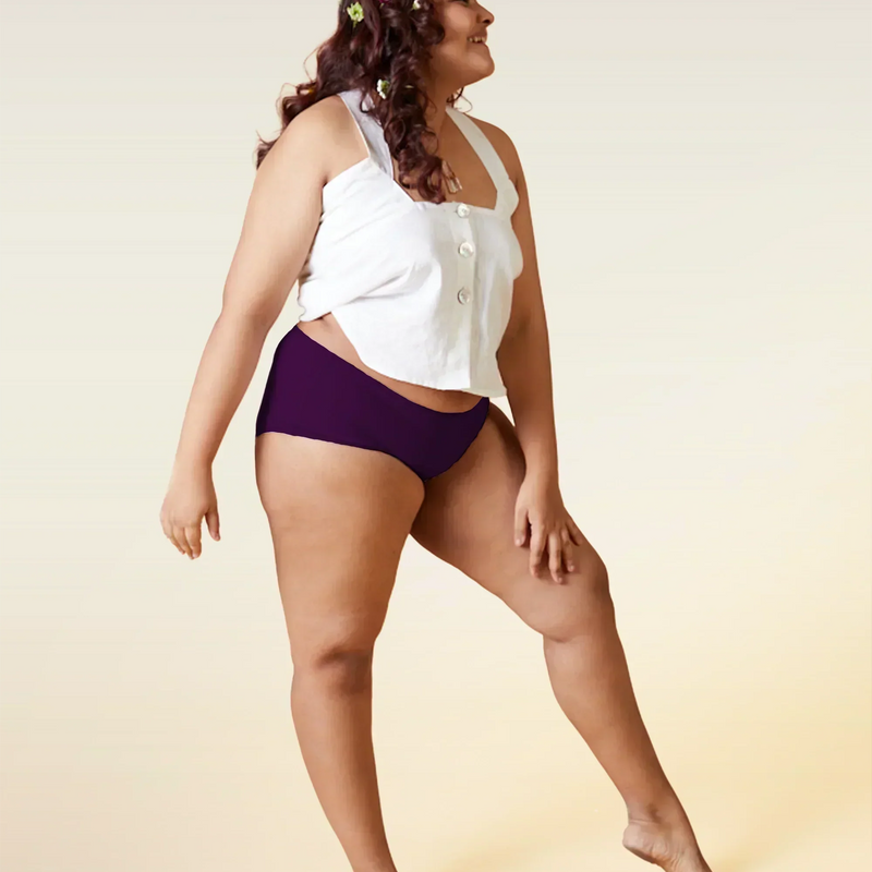 Woman wearing a white top and  violet mid-waist underwear on a beige background