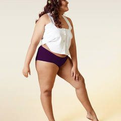 Woman wearing a white top and  violet mid-waist underwear on a beige background