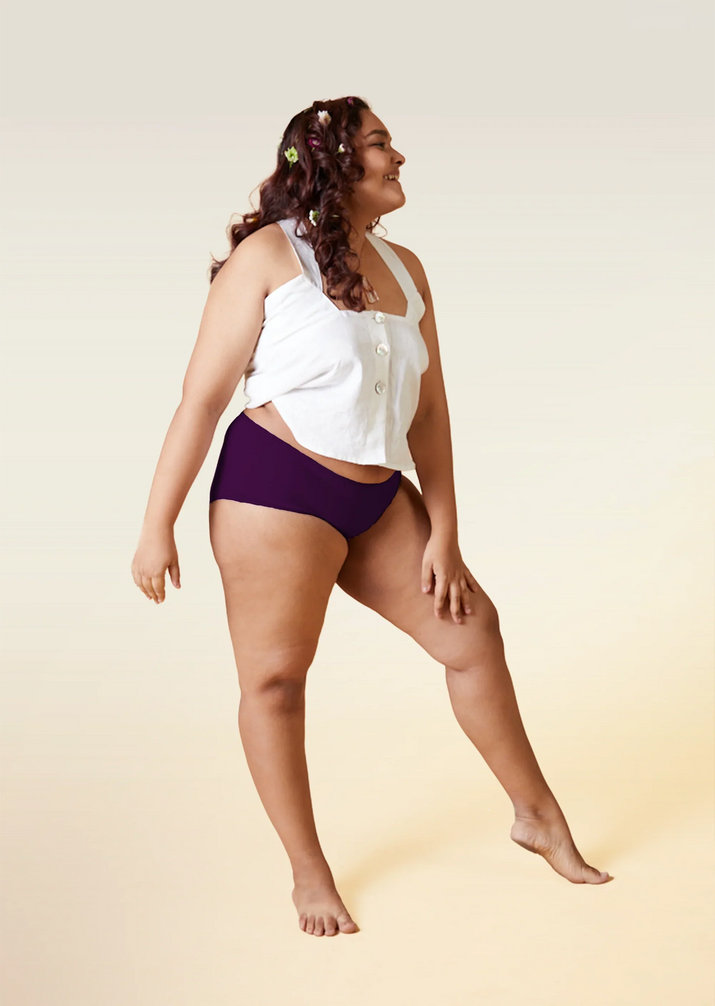 Woman wearing a white top and  violet mid-waist underwear on a beige background