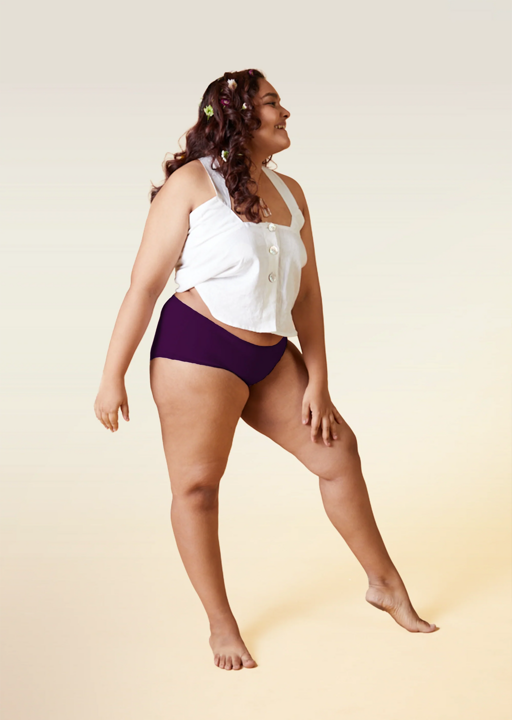 Woman wearing a white top and  violet mid-waist underwear on a beige background