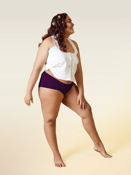 Woman wearing a white top and  violet mid-waist underwear on a beige background