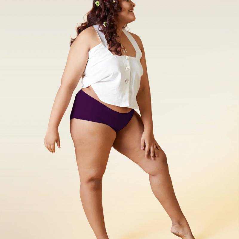 Woman wearing a white top and  violet mid-waist underwear on a beige background