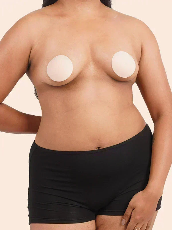 Person wearing a black underwear with silicone nipple patches on a beige background