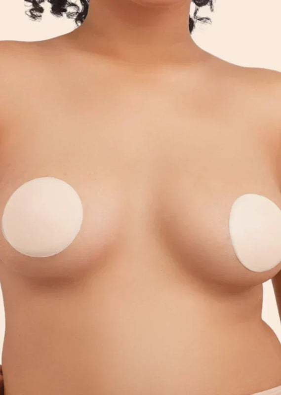 Close-up of a person's chest with silicone nipple covers on a plain background